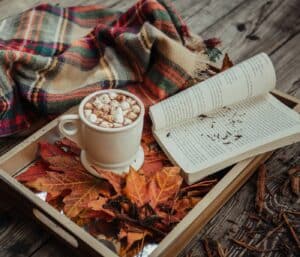 Ein Buch liegt auf einem Tablet, da neben steht eine Tasse mit heißer Schokolade und Marshmallows.