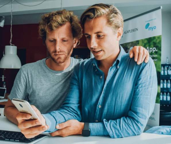 Felix & Jasper, die Gründer der Myo App, sehen sich die App auf dem Smartphone an