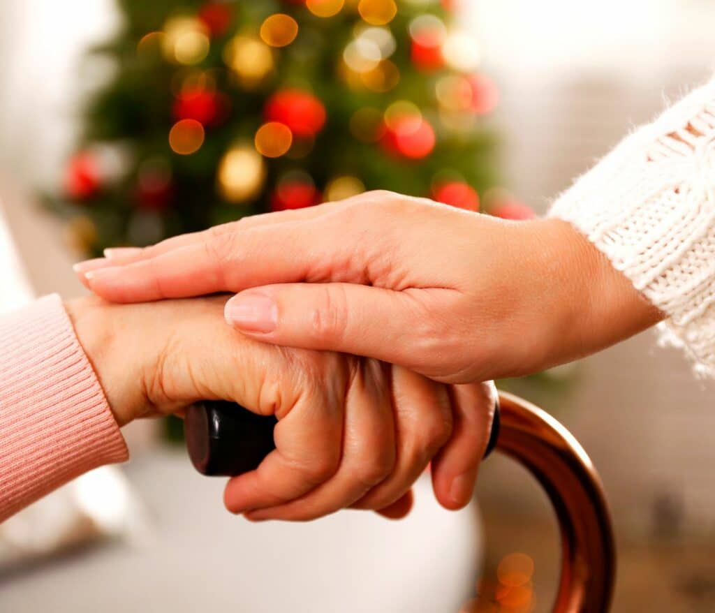 Symbolbild: Wie vereinen Pflegekräfte Job und die Familie an Weihnachten? : Zwei Hände im Vordergrund die aufeinandergelegt sind im Hintergrund ein Weihnachtsbaum