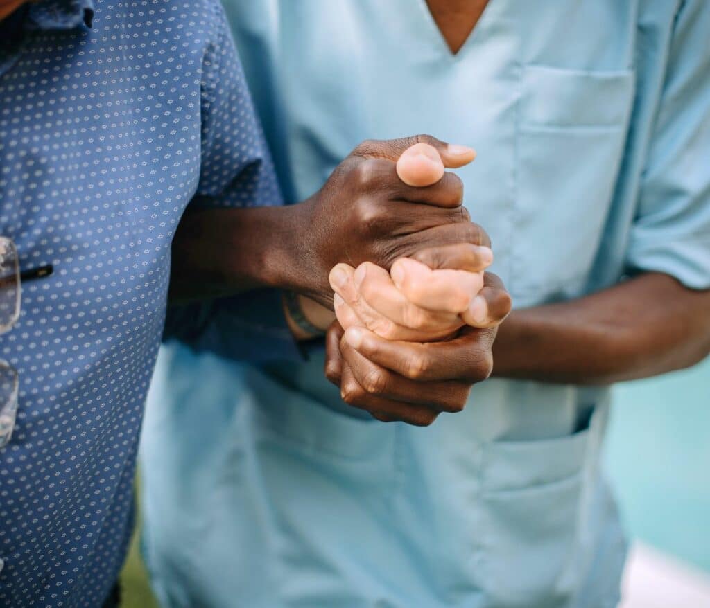 Symbolbild Anerkennung ausländischer Abschlüsse: Pflegekraft mit dunkler Hautfarbe hält hellfarbige Hände eines älteren Menschen