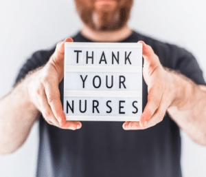 Symbolbild: Mangelnde Wertschätzung in der Pflege: Mann hält mit beiden Händen Schild in den Vordergrund, auf dem "Thank you Nurses" steht. Das Schild ist scharf im Vordergrund, der Mann ist unscharf zu sehen.